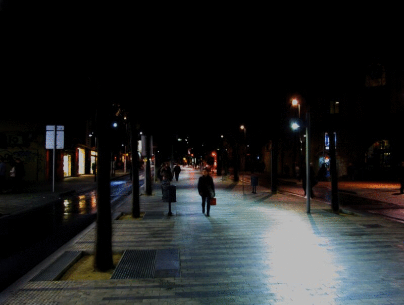 夜晚，行人在路灯闪烁的街道上行走图片下载