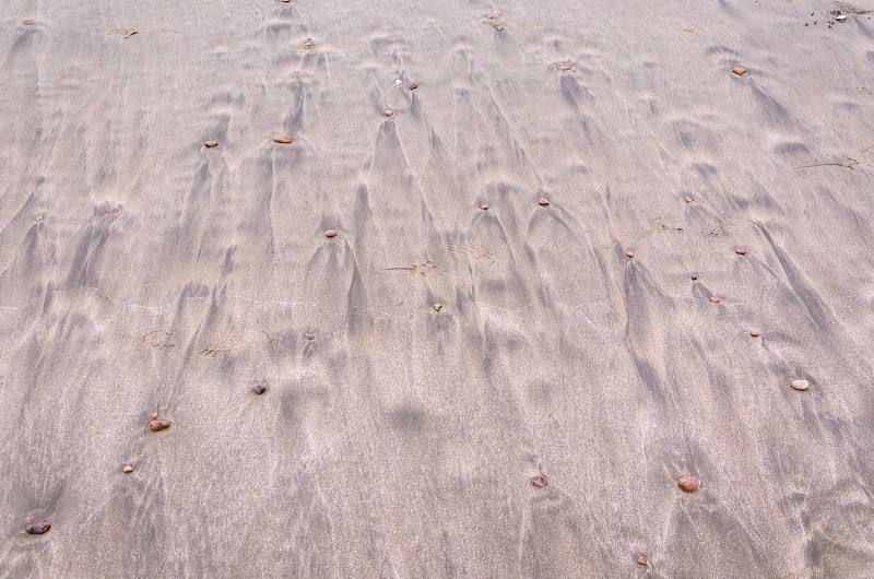 海浪冲刷后黄色海滩上石子后部形成的流水痕迹排列图案图片下载
