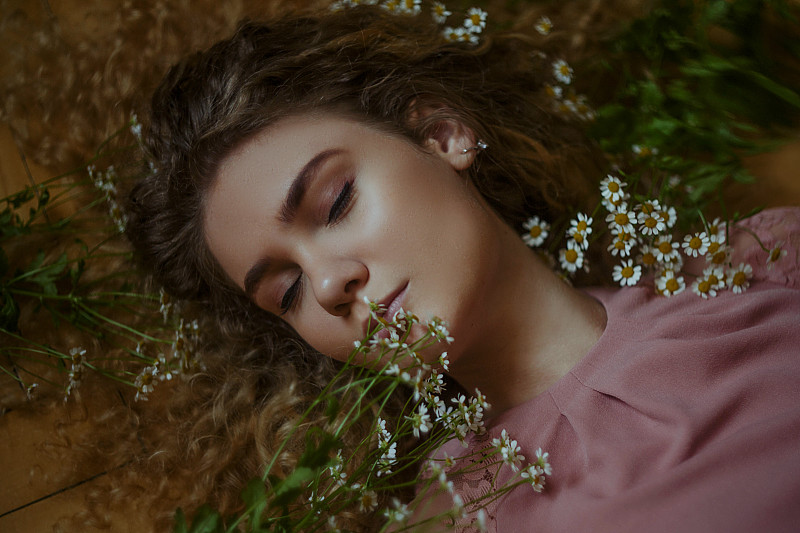 年轻女子睡在橙色的地面上，周围是鲜花图片下载