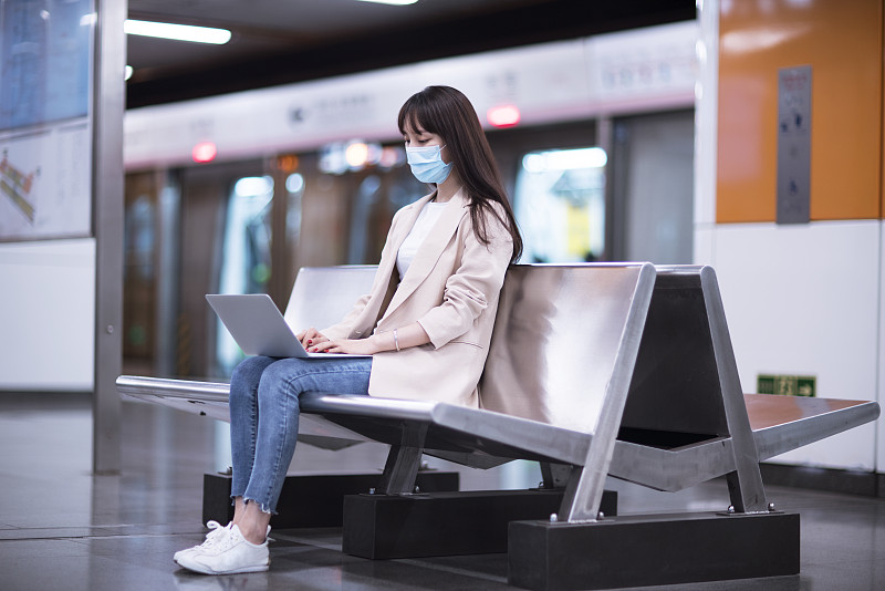 年轻商务女士戴着防护口罩在地铁站使用笔记本电脑工作图片素材