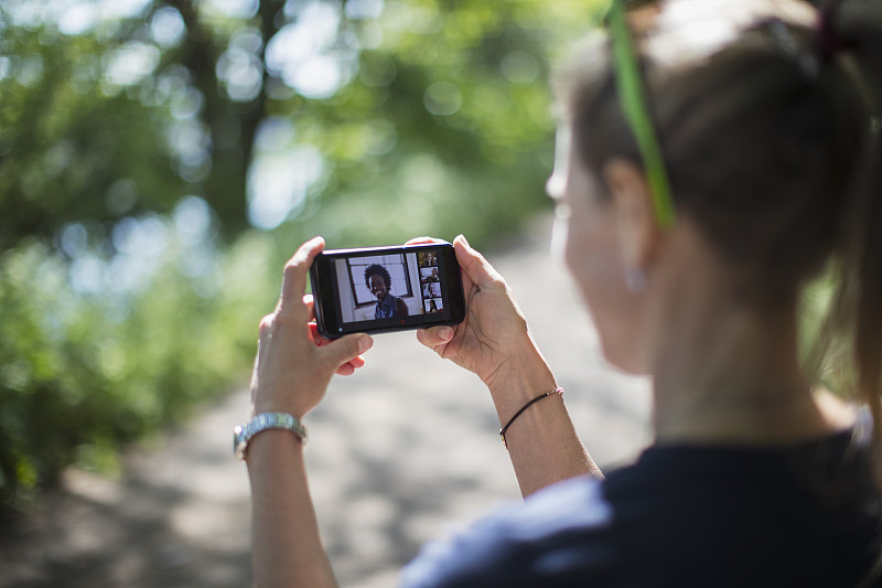 一名女子在阳光明媚的公园里用智能手机屏幕与朋友视频聊天图片下载