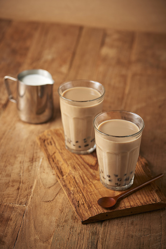 木制托盘上放着两杯带珍珠粉的棕色奶茶，牛奶旁边放着勺子图片下载