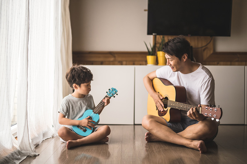 特写的小男孩和父亲坐在旁边的幕布弹吉他图片下载