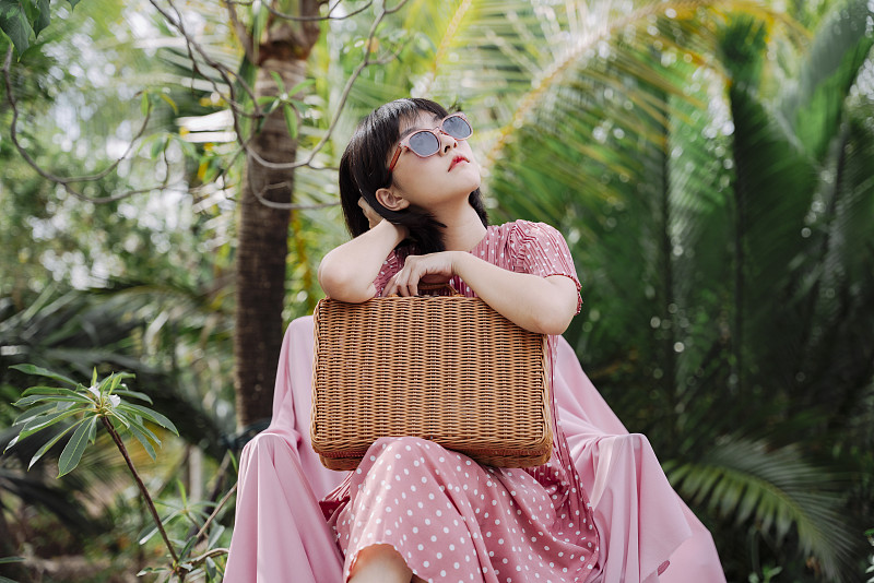 美丽的亚洲泰国女人短深色头发在粉红色连衣裙戴太阳镜坐在沙发上野餐篮子。图片下载