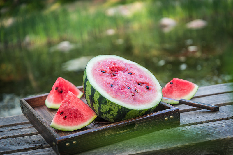 夏季户外水边木桌上切开的冰镇西瓜图片下载