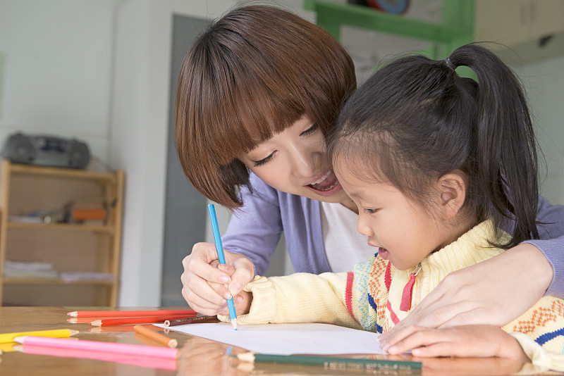 Kindergarten teacher and girl writing图片下载