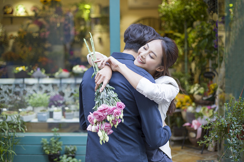 年轻女子手拿鲜花拥抱男朋友图片下载