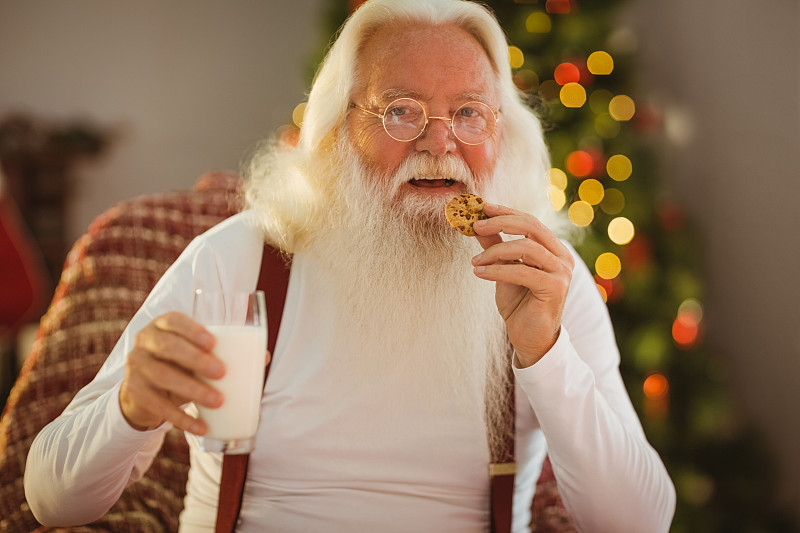 微笑的圣诞老人在家里的客厅吃饼干图片下载