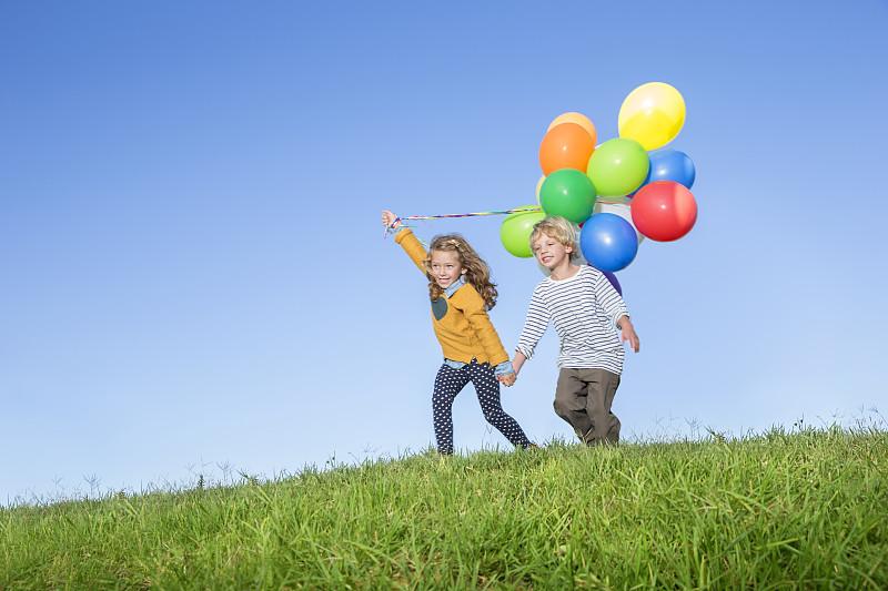 在长满草的小山上，孩子们拿着一堆气球图片下载