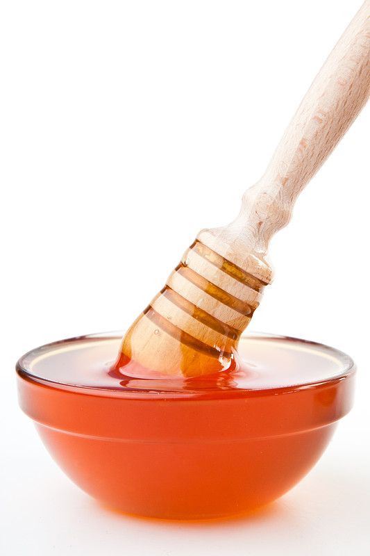 蜂蜜勺到表面上的蜂蜜碗在白色的背景图片素材