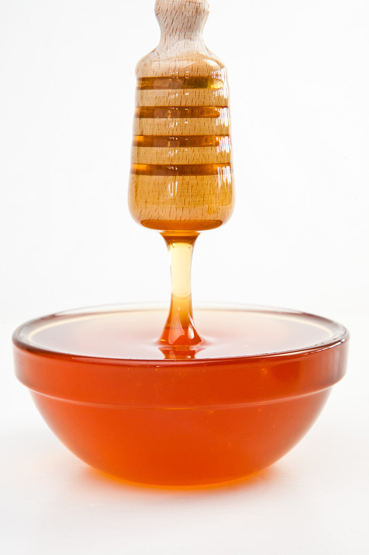细细的蜂蜜在白色的背景下滴落在装满蜂蜜的碗里图片素材