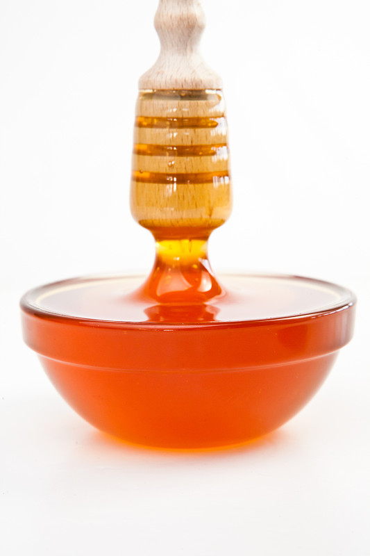 在白色的背景下，蜂蜜在装满蜂蜜的碗里垂直滴落图片下载