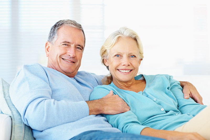 一对微笑的退休夫妇坐在家里的沙发上图片下载