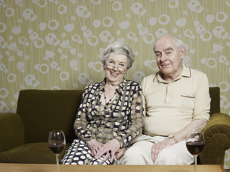 丈夫和妻子在沙发上休息，两杯红酒放在前面的桌子上图片下载