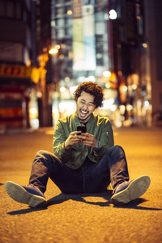 一名年轻的日本少年晚上在户外拿着手机微笑图片下载