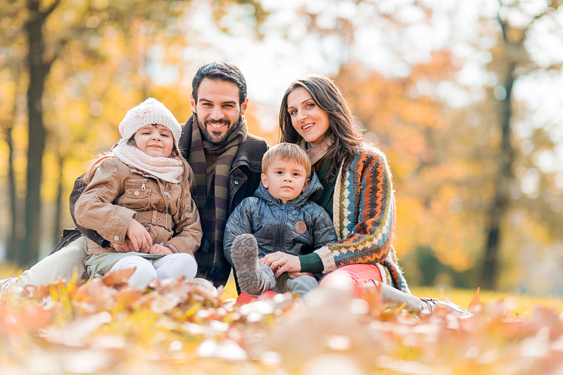 一家人在公园里微笑着欣赏秋叶。图片下载