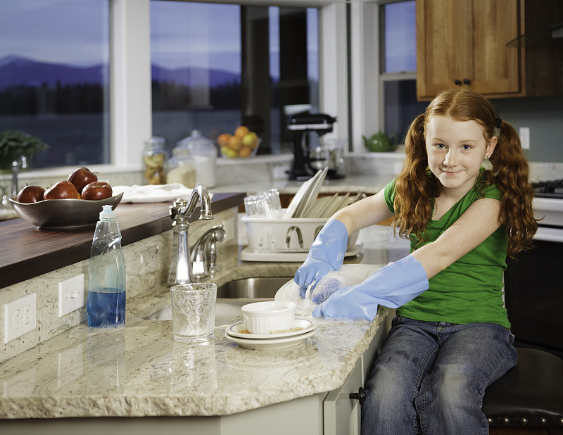 小红发女孩微笑着在晚上厨房洗盘子图片素材