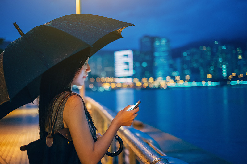 在城市里用智能手机撑伞的女性图片下载
