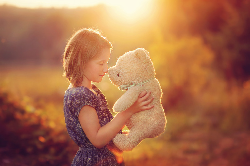 一个小女孩在阳光下举着她的泰迪熊图片下载