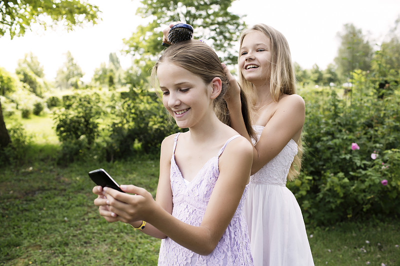 一个女孩在用手机，而她姐姐在给她梳头图片下载