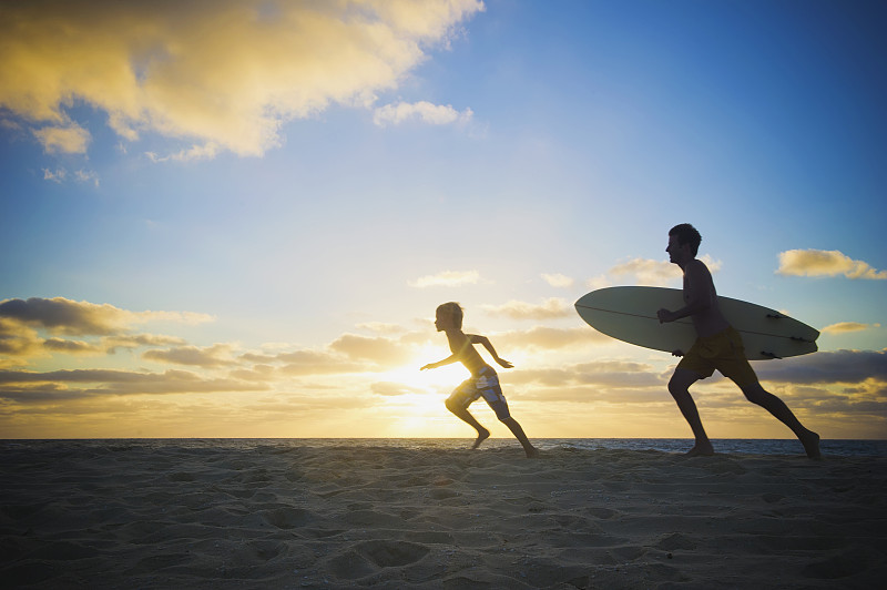 白人父亲和儿子在海滩上玩冲浪板图片下载