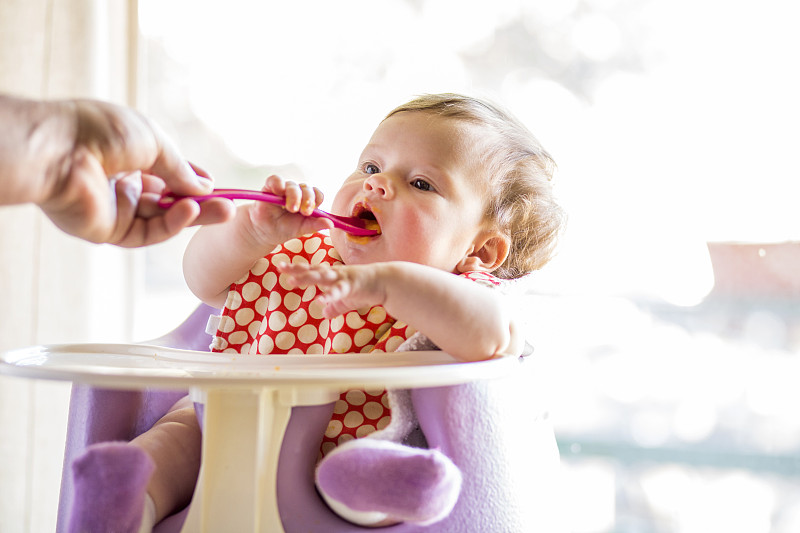 白人女婴在高椅上用勺子吃东西图片下载