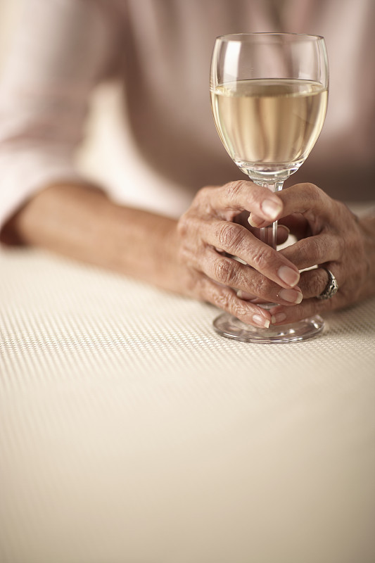 老妇人坐着，手里拿着一杯白葡萄酒，中间部分，手的特写图片下载