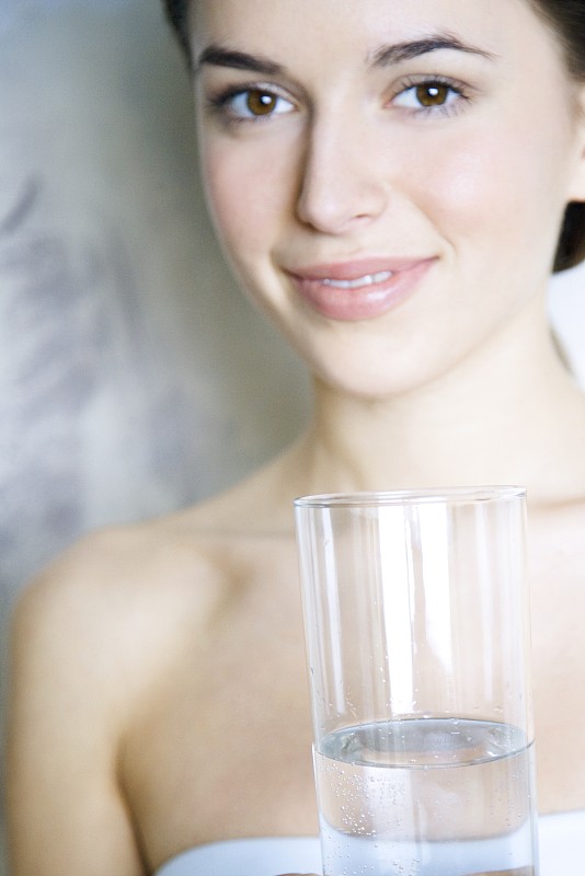 年轻女子拿着一杯水，对着镜头微笑图片下载