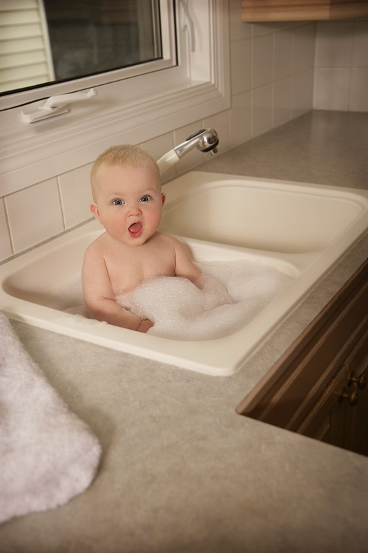 一个婴儿在厨房的水槽里洗澡图片下载