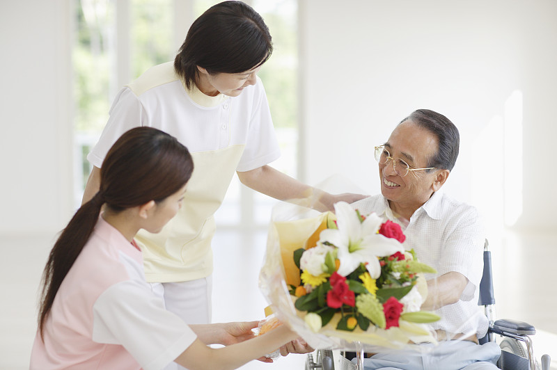 护理人员向坐在轮椅上的老人献上一束鲜花图片下载