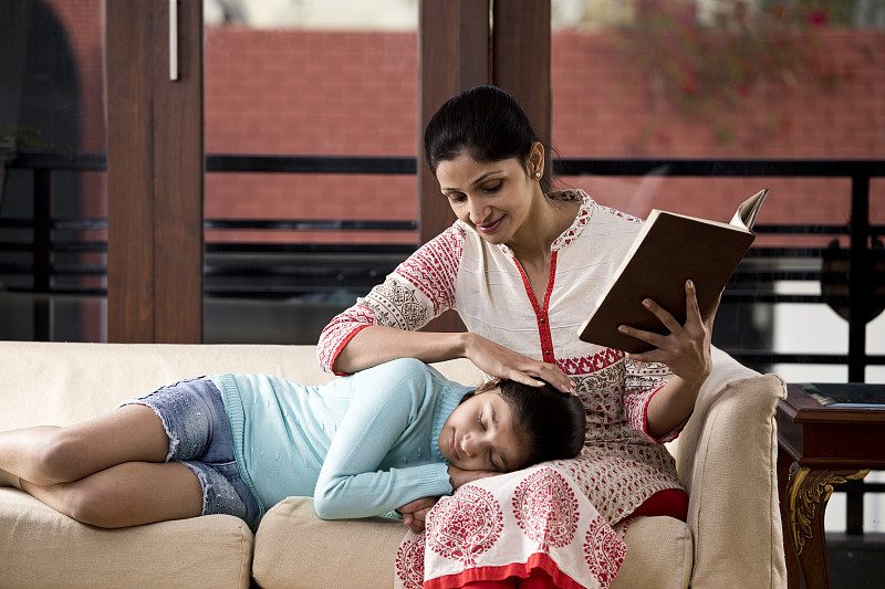 一个女人在看书，女儿睡在她的腿上图片素材
