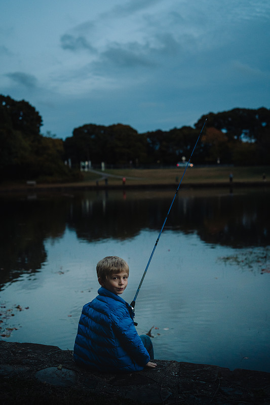 一个小男孩晚上钓鱼。图片素材