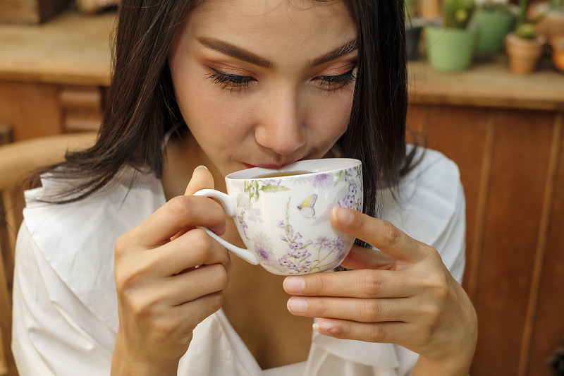 美丽的女人喝热茶在咖啡馆，头部特写图片素材