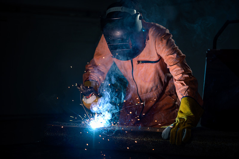 在管道工作中带保护面罩和火花的焊接金属的工业焊工图片素材