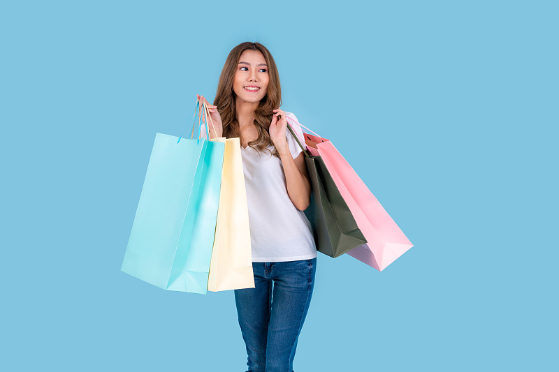 美丽迷人的亚洲女人微笑着，拿着购物袋感觉如此幸福，享受黑色星期五在购物中心的销售，孤立在青色的背景。图片下载