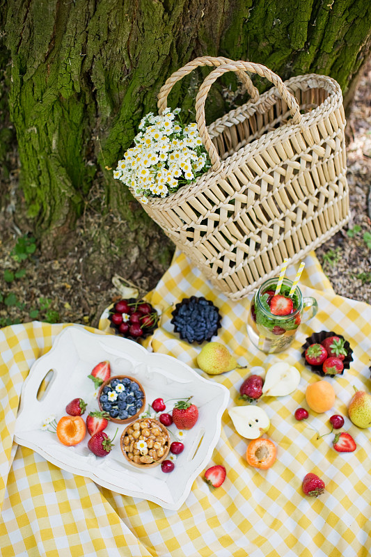 在公园野餐。白色木托盘上放着新鲜水果和果馅饼，草袋里放着白色甘菊图片下载