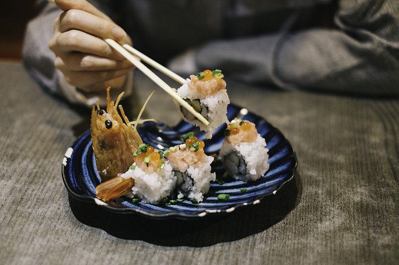 一位年轻的亚洲女商人下班后在日本餐馆用筷子吃寿司图片素材