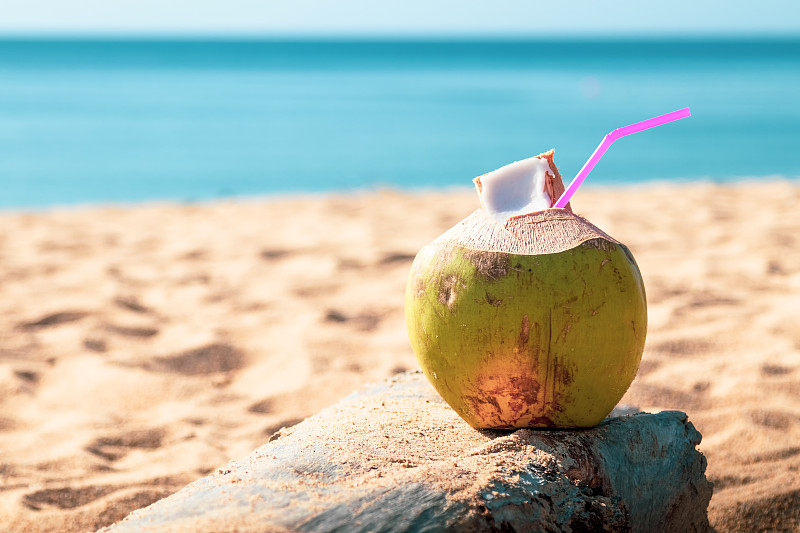 甜美的绿色椰子水和饮用稻草在泰国普吉岛的沙滩上。图片下载