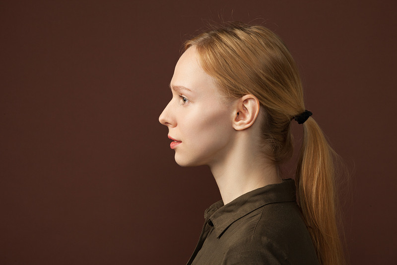 一名25岁女性在棕色背景上的工作室肖像图片素材