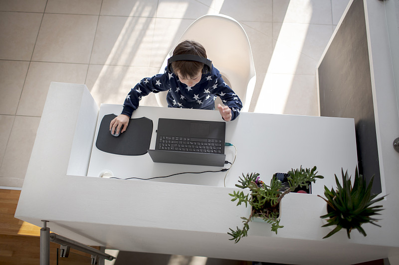 俯视图男孩坐在家里的书桌上戴着耳机和使用笔记本电脑图片素材