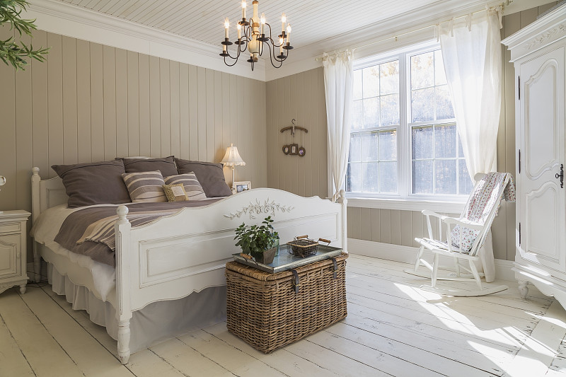 双人床，奶油色地板，棕色木镶板墙，白色家具和窗帘。图片素材