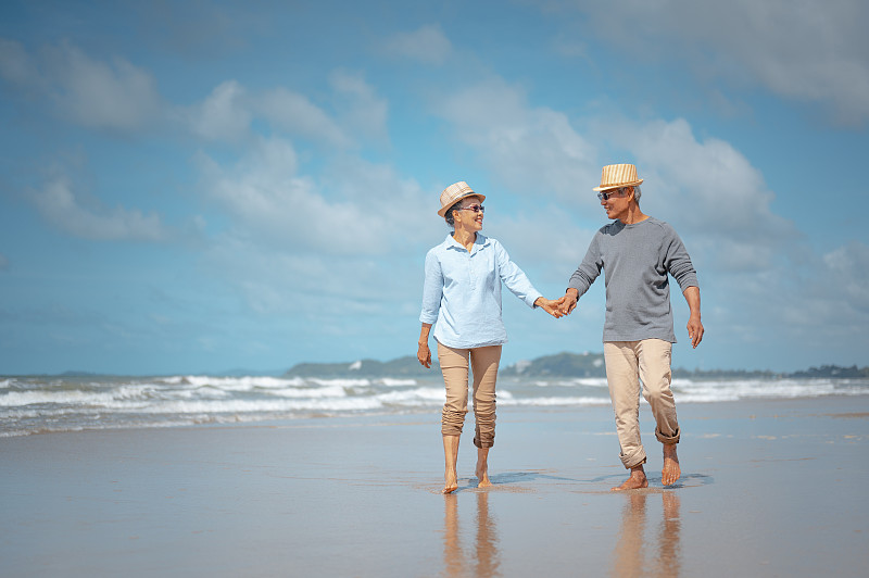 一对老年夫妇在海滩上牵手散步图片素材