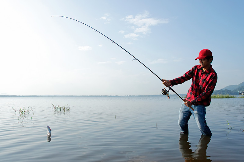 渔夫站在湖里，用钓竿钓鱼图片素材