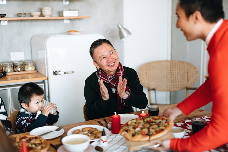 快乐的亚洲多代家庭花时间一起庆祝圣诞节，微笑的年轻人在圣诞派对期间在家里为家人服务食物图片素材