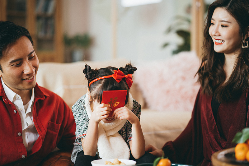 快乐的年轻亚洲家庭庆祝春节，父母给他们的女儿红包，她接受他们的双手图片素材