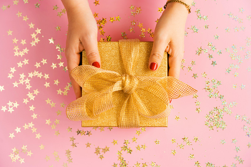 女人的手拿着一个绿色的礼品盒与黄色缎带在粉红色的背景图片下载