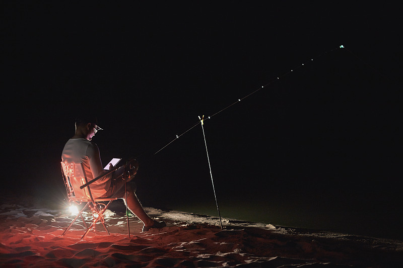 一个渔民晚上在河岸上用喂食器捕鱼。图片素材