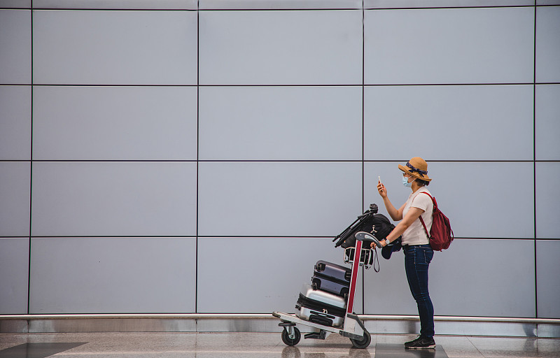 一名亚洲妇女推着行李车在机场候机厅打电话图片下载