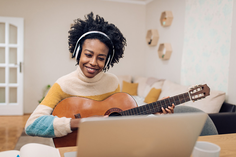 年轻的非洲裔美国妇女使用在线教程学习弹吉他图片下载