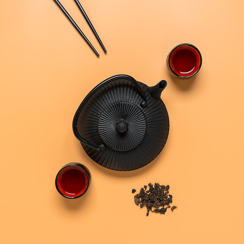 亚洲传统茶道的创意布局。粉彩背景上的黑色金属茶壶、陶瓷茶杯和筷子。前视图。图片下载